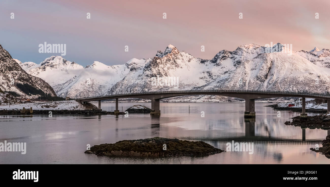 Un pont au-dessus de l'eau tranquille avec nuage rose sur le robuste, montagnes couvertes de neige, Nordland, Norvège Banque D'Images
