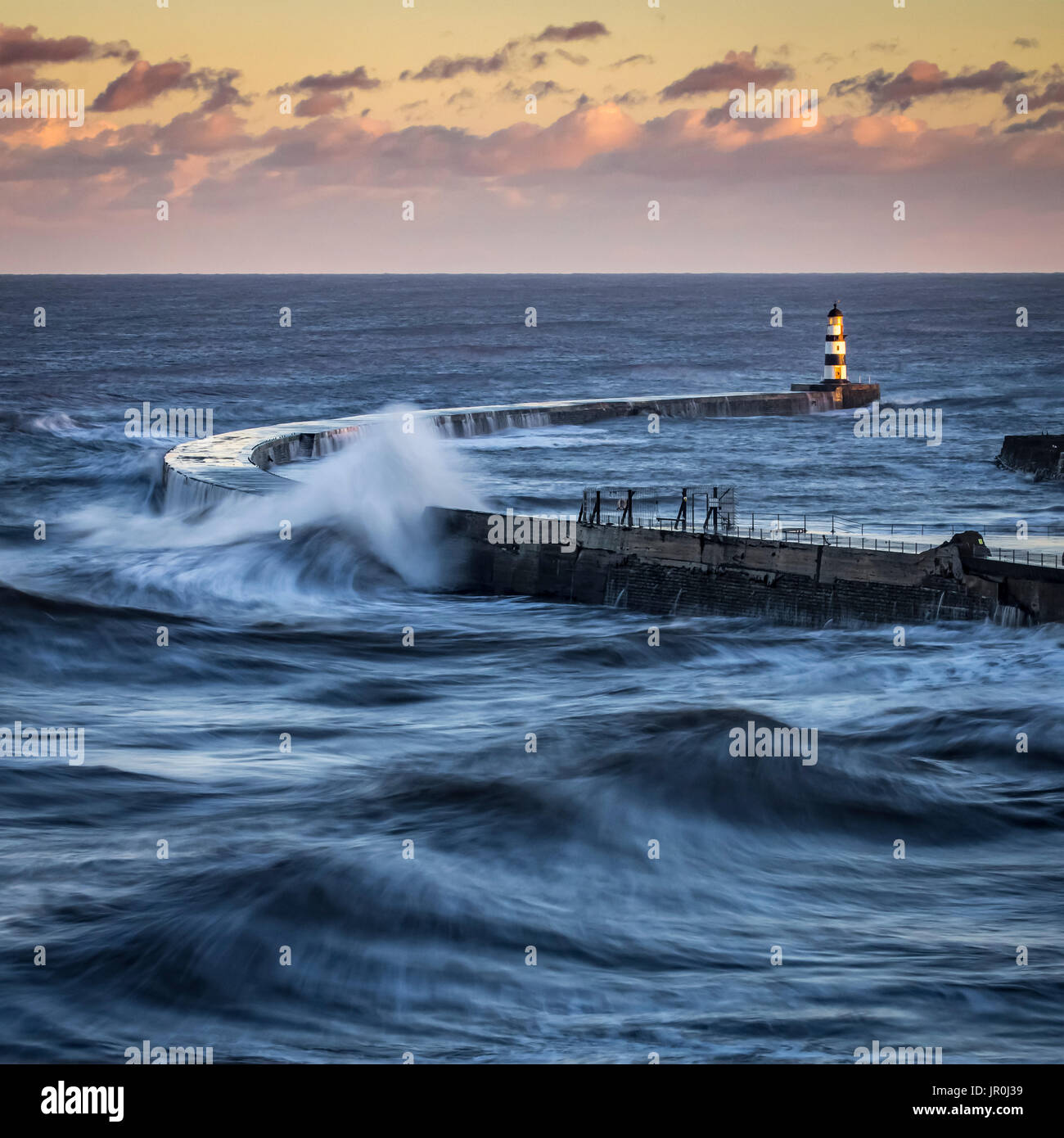 Éclaboussures des vagues sur la jetée avec un ciel rougeoyant au coucher du soleil ; Seaham, County Durham, Angleterre Banque D'Images