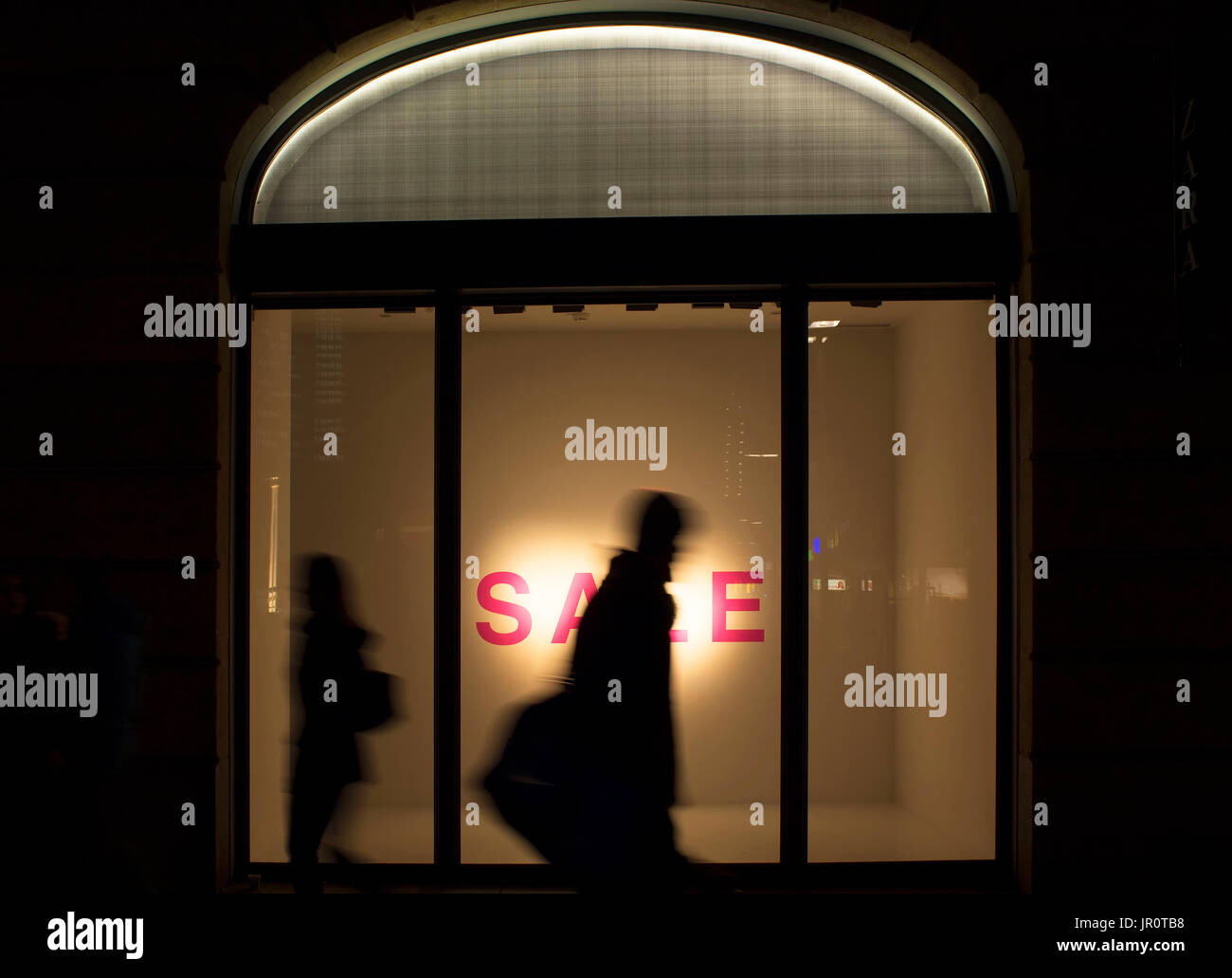 Silhouettes d'homme et de la femme en marche motion floue devant une vitrine du magasin de mode dans la nuit. Image conceptuelle de la saison de vente, de la consommation et Banque D'Images