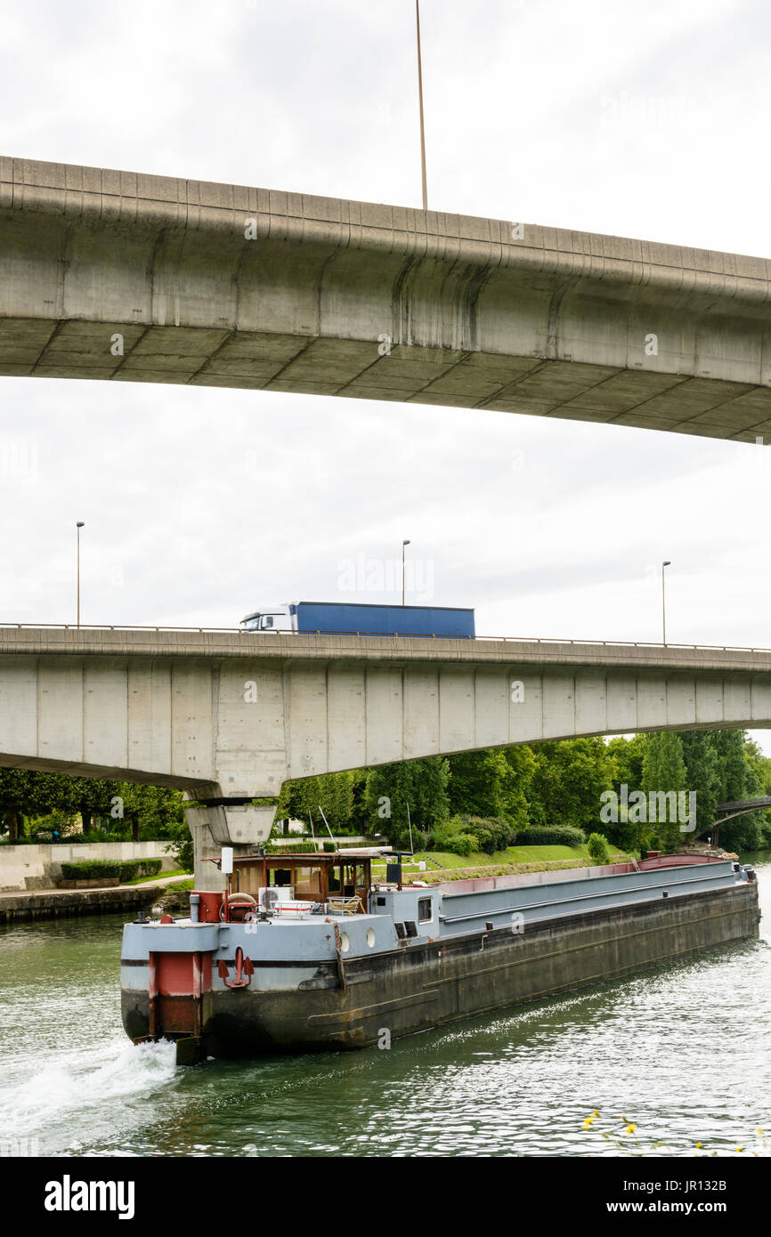 Une barge de fret vides en descendant la rivière Marne en direction de Paris alors qu'un semi-remorque chariot roule sur une rampe de l'autoroute A86 sur la voie navigable. Banque D'Images