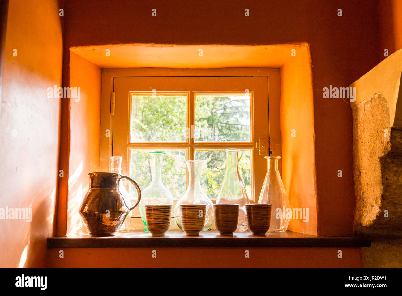 Petite fenêtre avec des bouteilles, jug et tasses dans une vieille maison en pierre, de couleur orange sur les murs anciens. Banque D'Images