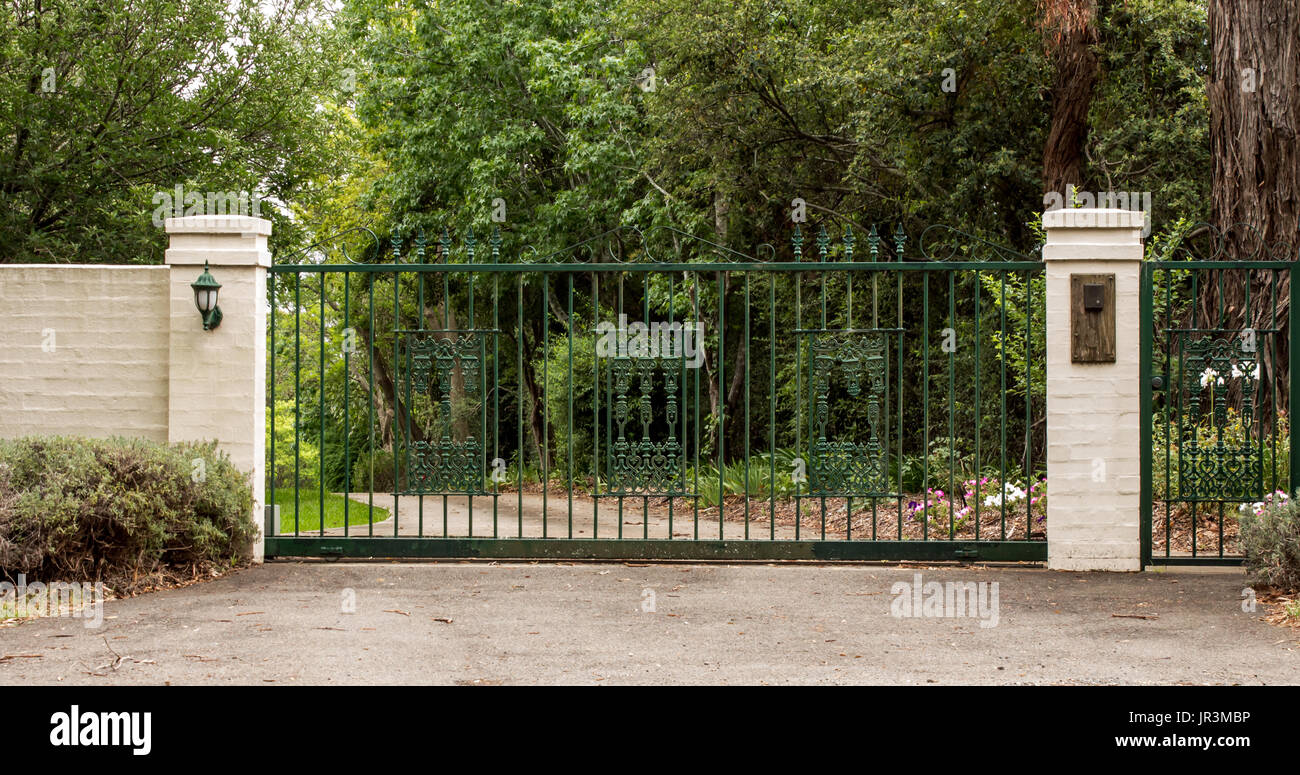 Metal entrée vannes réglées en brique clôture avec jardin arbres en arrière-plan Banque D'Images