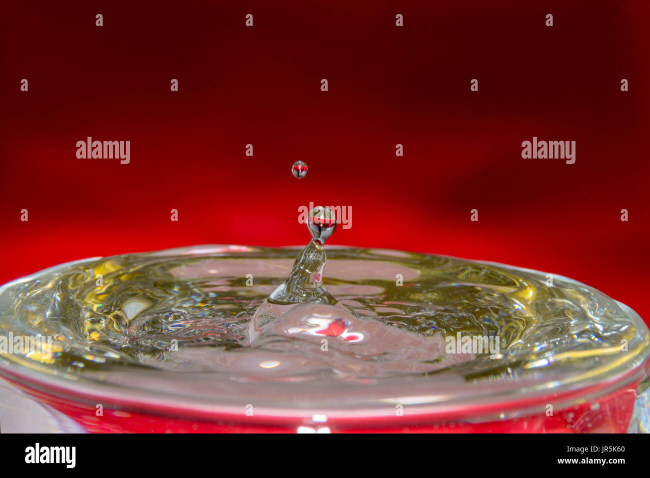 Gota de agua con fondo Rojo y reflejo dorado en el agua, bebida rafraîchissante y fría con ondas de impacto en el agua, gota que derrama el Vaso con Agua Banque D'Images