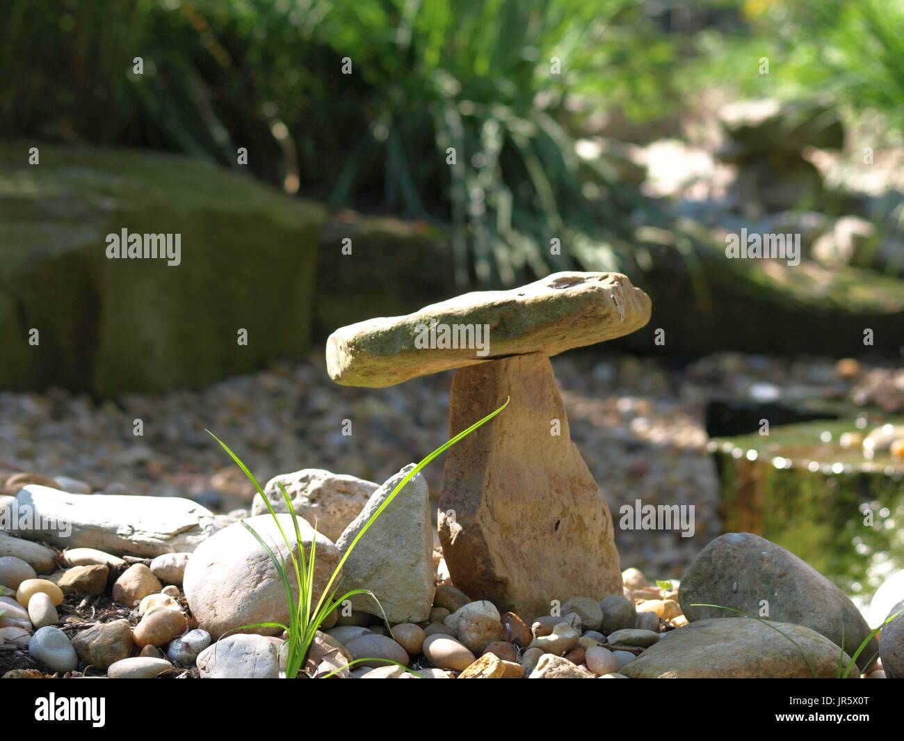 Jardin zen rock en équilibre sur un autre rocher, avec des brins d'herbe en premier plan Banque D'Images