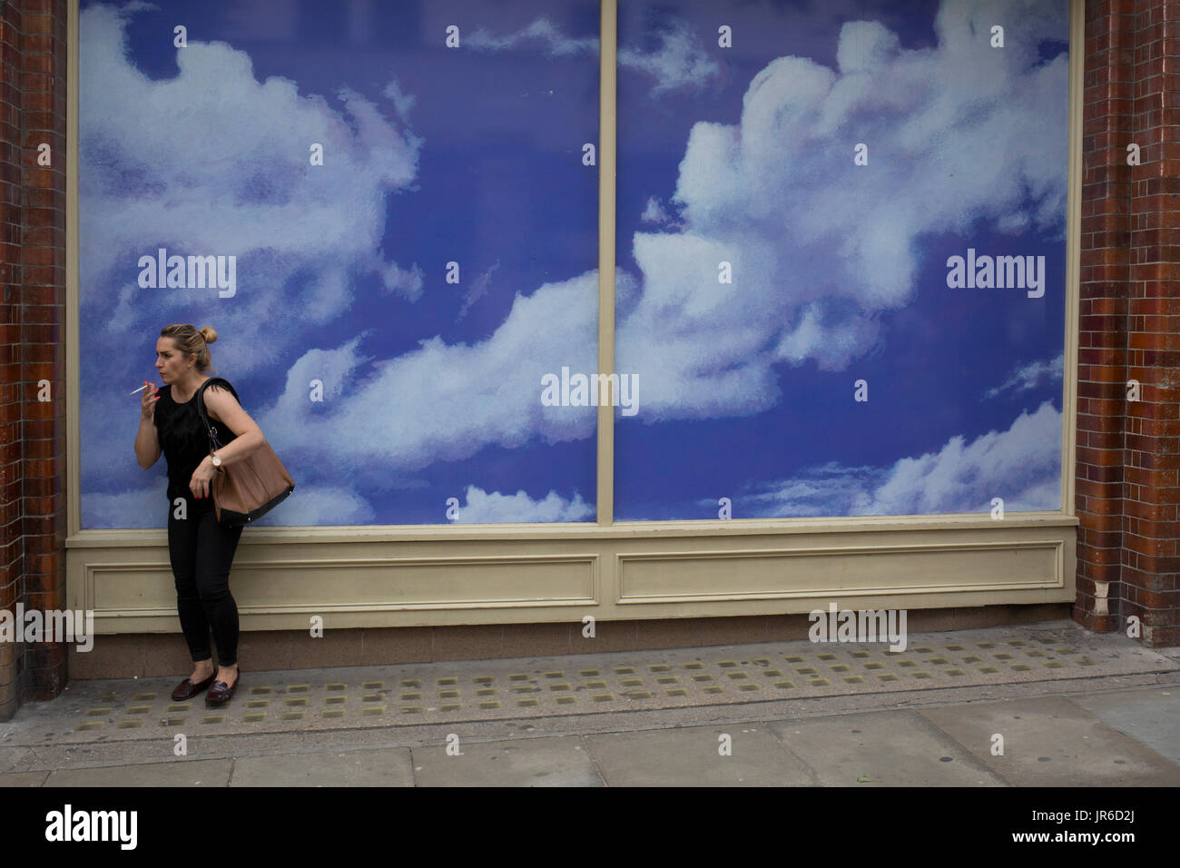 Un fumeur se trouve en face d'une thésaurisation de construction avec cloud et sky, le 31 juillet 2017, à Covent Garden, Londres, Angleterre. Banque D'Images