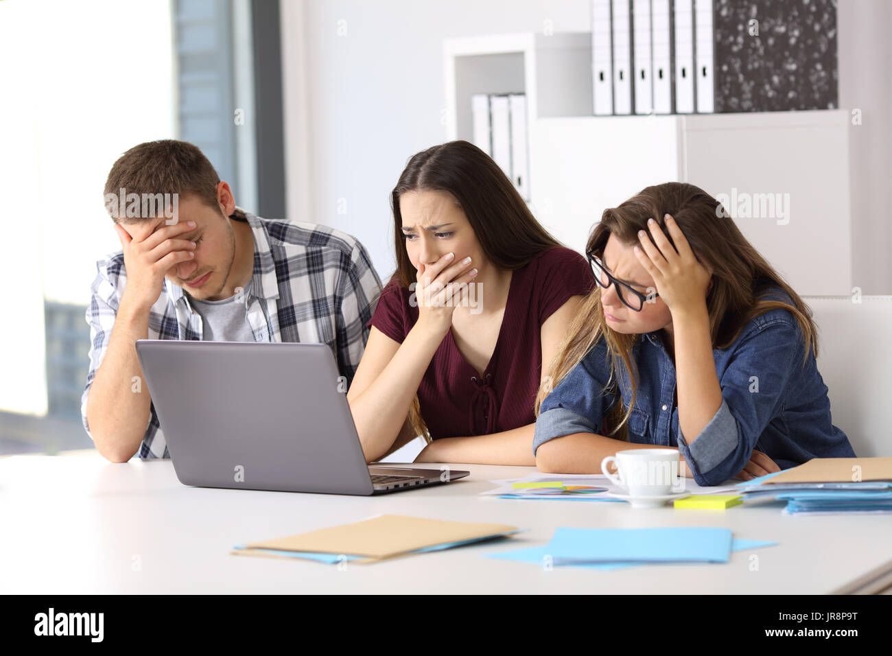 Trois entrepreneurs inquiets d'avoir l'oeil sur le contenu en ligne dans un laptop at office Banque D'Images