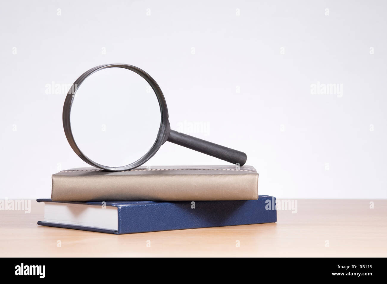 Loupe en équilibre sur le haut de deux livres à couverture rigide avec copie espace sur un mur blanc au-dessus d'une table en bois Banque D'Images