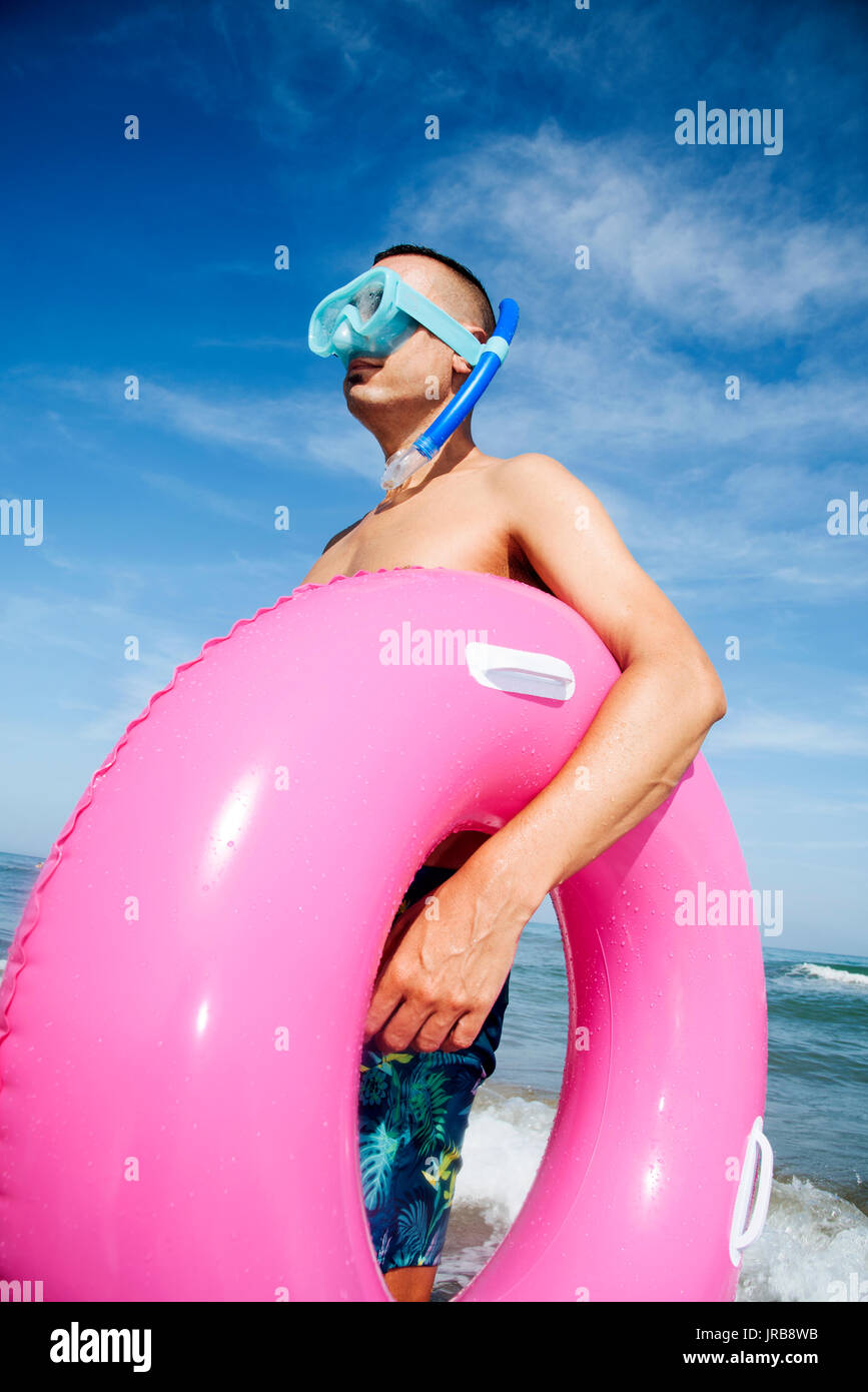 Closeup of a young caucasian homme portant un masque de plongée, un tuba et un anneau de bain rose sur la plage Banque D'Images