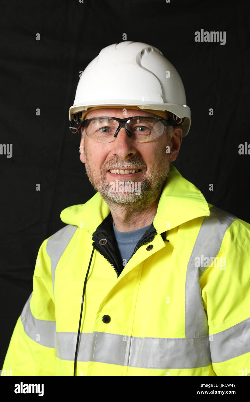 Un ouvrier du bâtiment en veste jaune à haute visibilité sourit à la caméra. Fond sombre Uni. Banque D'Images