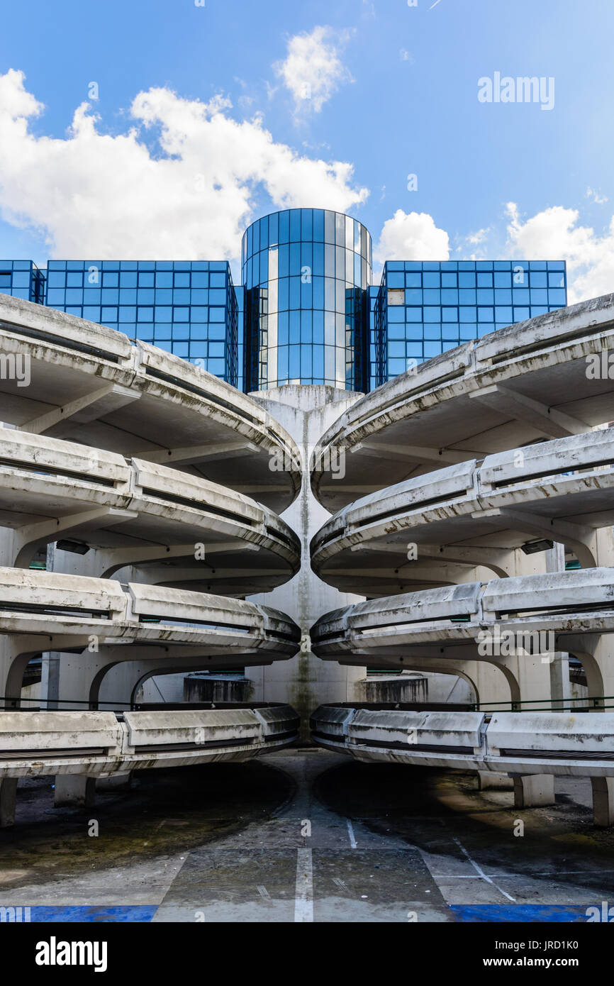 Rampes d'accès en spirale d'un vieux béton décrépit de parking, avec un immeuble de bureaux en verre à l'arrière-plan. Banque D'Images