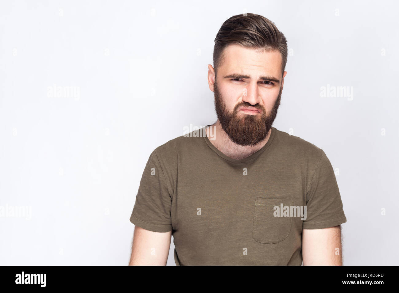 Portrait d'homme barbu triste malheureux avec t-shirt vert foncé à l'arrière-plan gris clair. studio shot. Banque D'Images