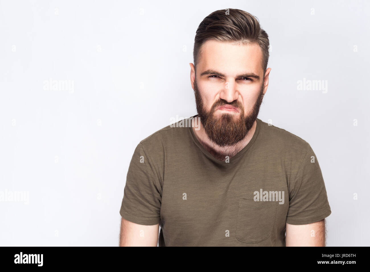 Portrait d'homme barbu triste en colère avec t-shirt vert foncé à l'arrière-plan gris clair. studio shot. Banque D'Images
