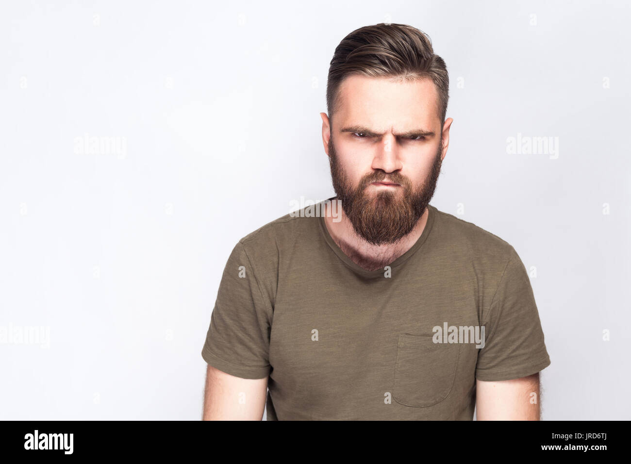 Portrait d'homme barbu triste en colère avec t-shirt vert foncé à l'arrière-plan gris clair. studio shot. Banque D'Images