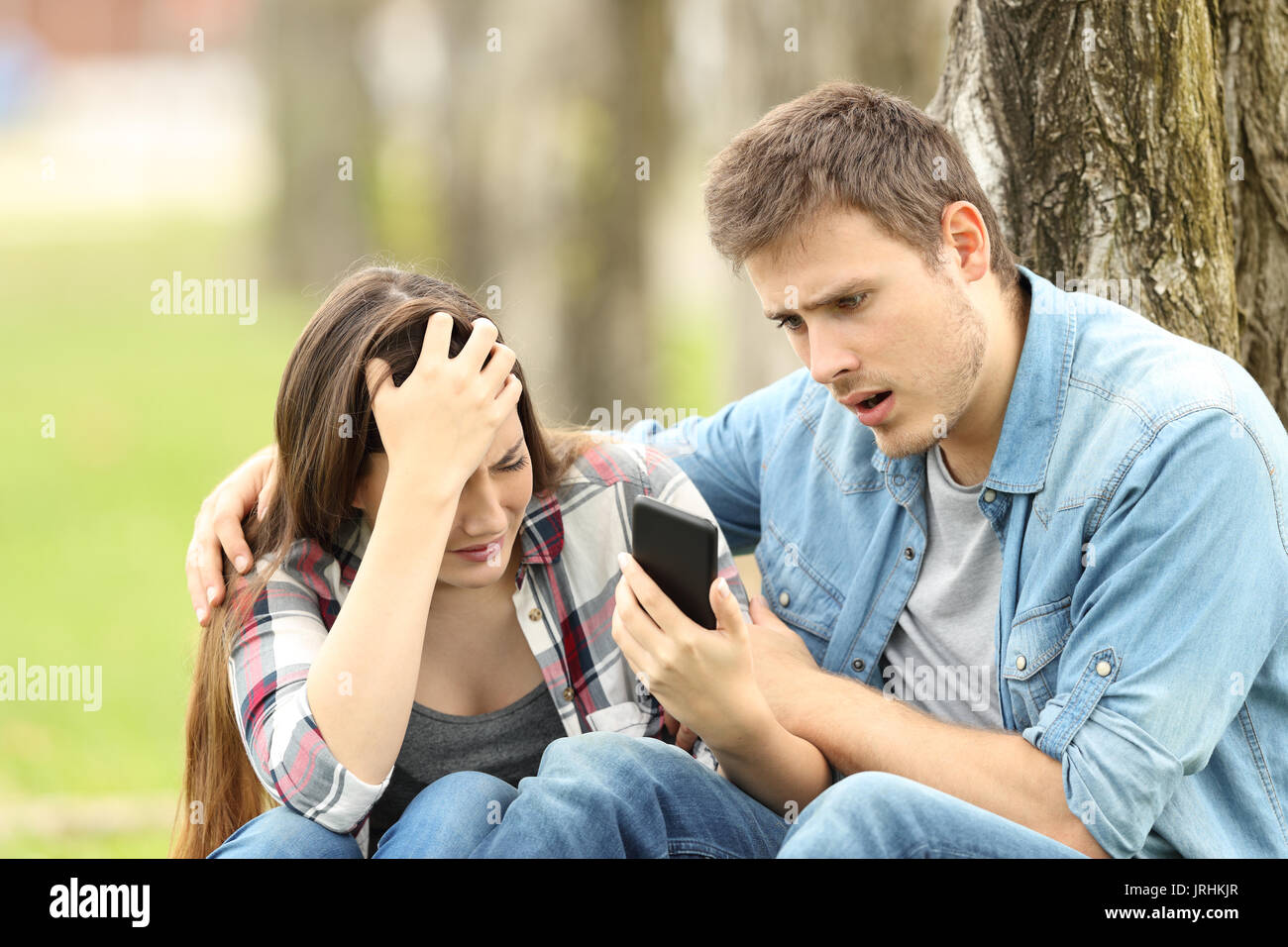 Montre Femme triste message négatif à un ami surpris assis sur l'herbe dans un parc Banque D'Images