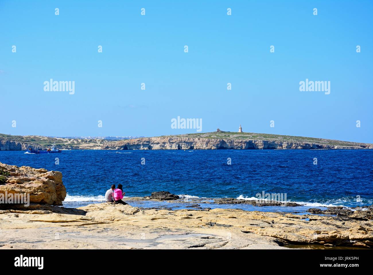 Un couple assis sur le rivage rocheux avec vue sur la baie, Bugibba, Malte, l'Europe. Banque D'Images