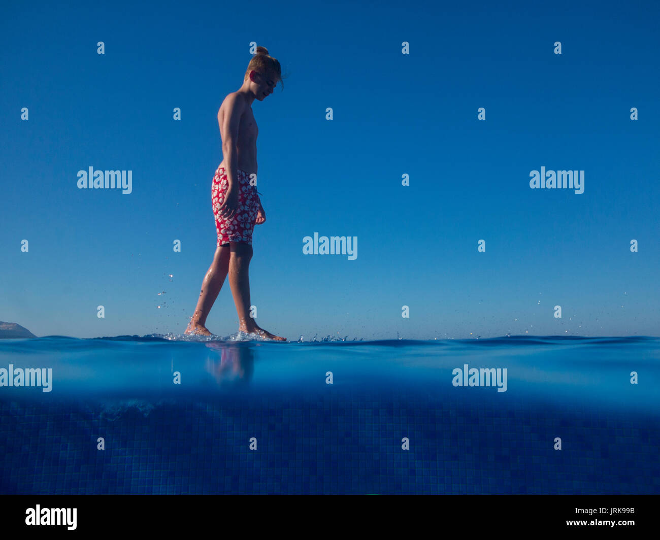 Ennuyer un adolescent marche sur le bord d'une piscine à débordement en vacances Banque D'Images