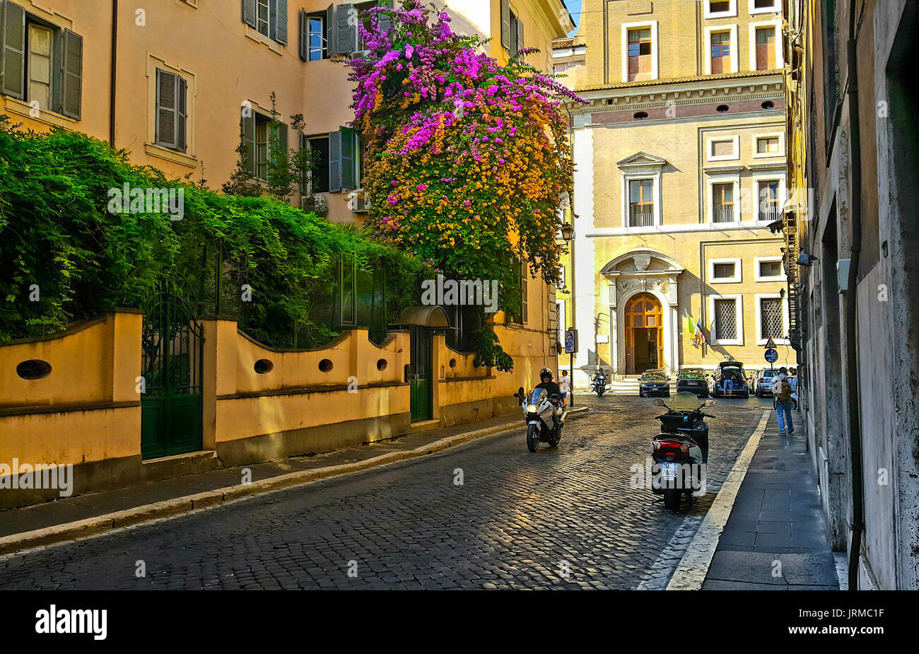 Rue de Rome avec un bougainvilliers colorés avec des fleurs rose et orange sur le côté d'un immeuble avec une moto et un solo traveler Banque D'Images