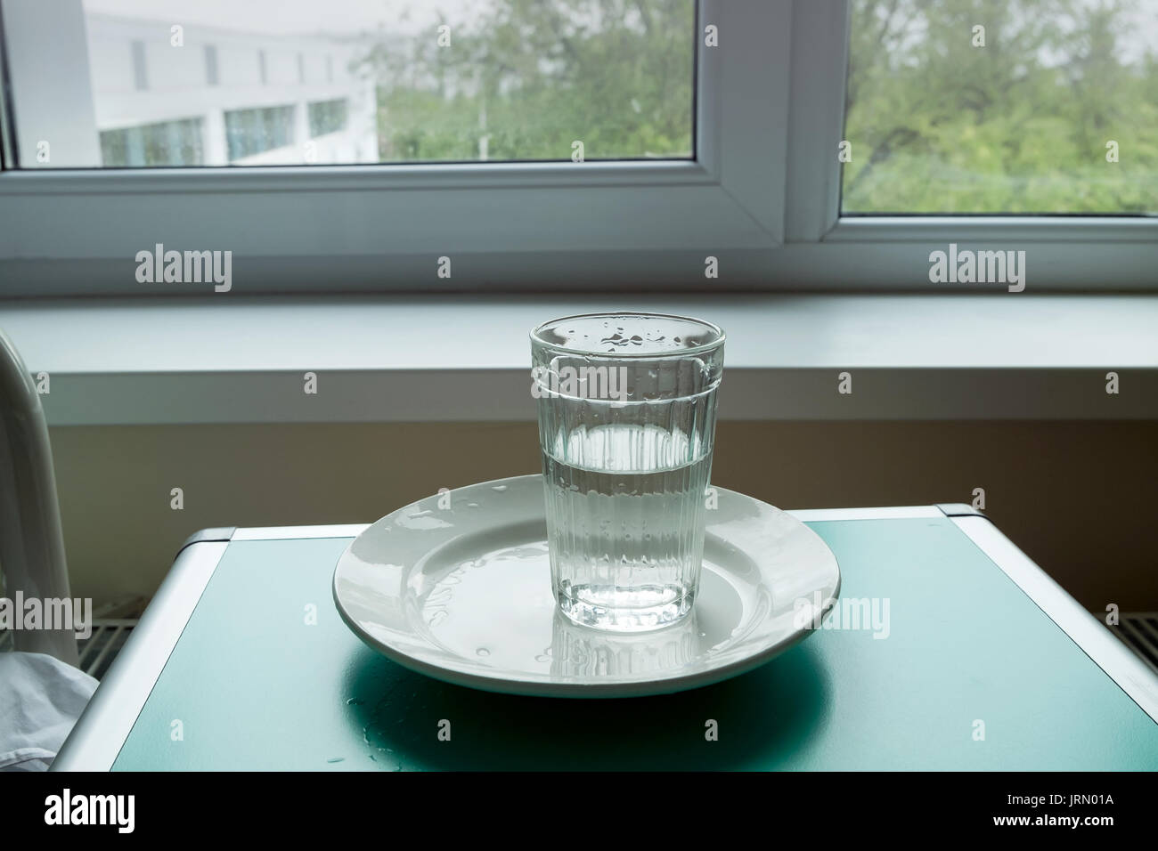 Verre d'eau sur une plaque dans la chambre de l'hôpital. - Horizontal le  verre avec de l'eau remplie à demi et un lit d'hôpital avec un oreiller  triangulaire Photo Stock - Alamy