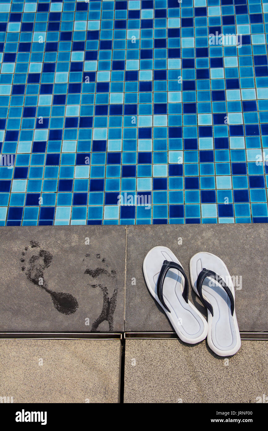 Paire de tongs bleu et empreintes de pas sur le côté piscine Banque D'Images