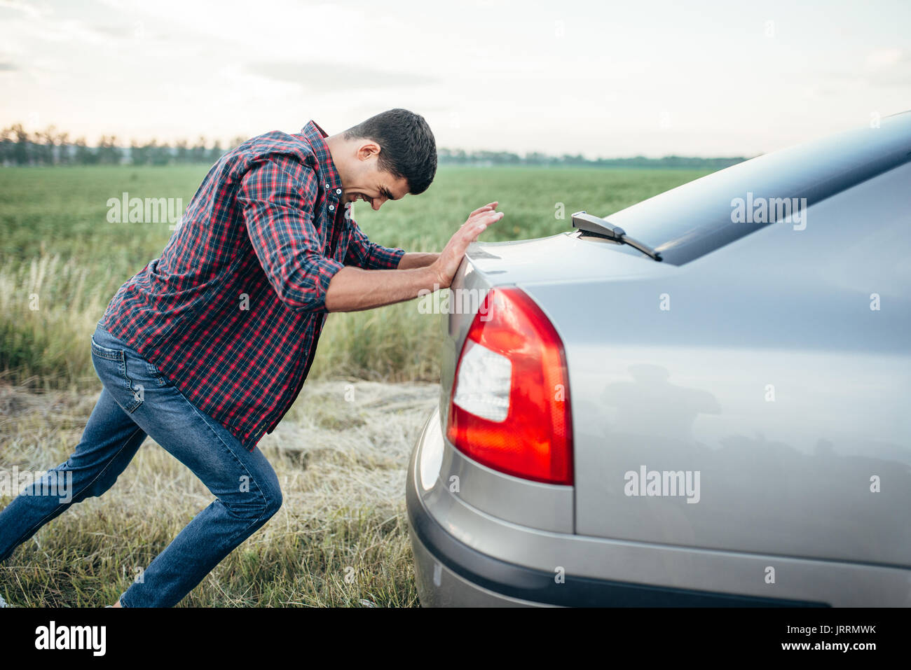 Man pushing casse voiture, vue de côté. Véhicule avec trounble sur route au jour d'été Banque D'Images