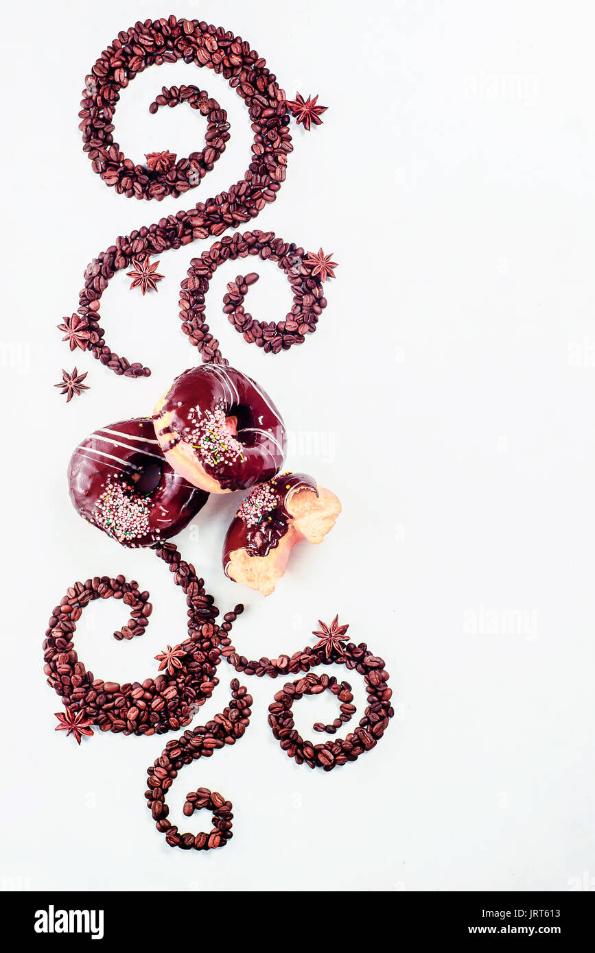 Les grains de café allongé en forme d'un tourbillon avec la coupe, la cannelle, l'anis étoile et les beignes sur un fond blanc Banque D'Images