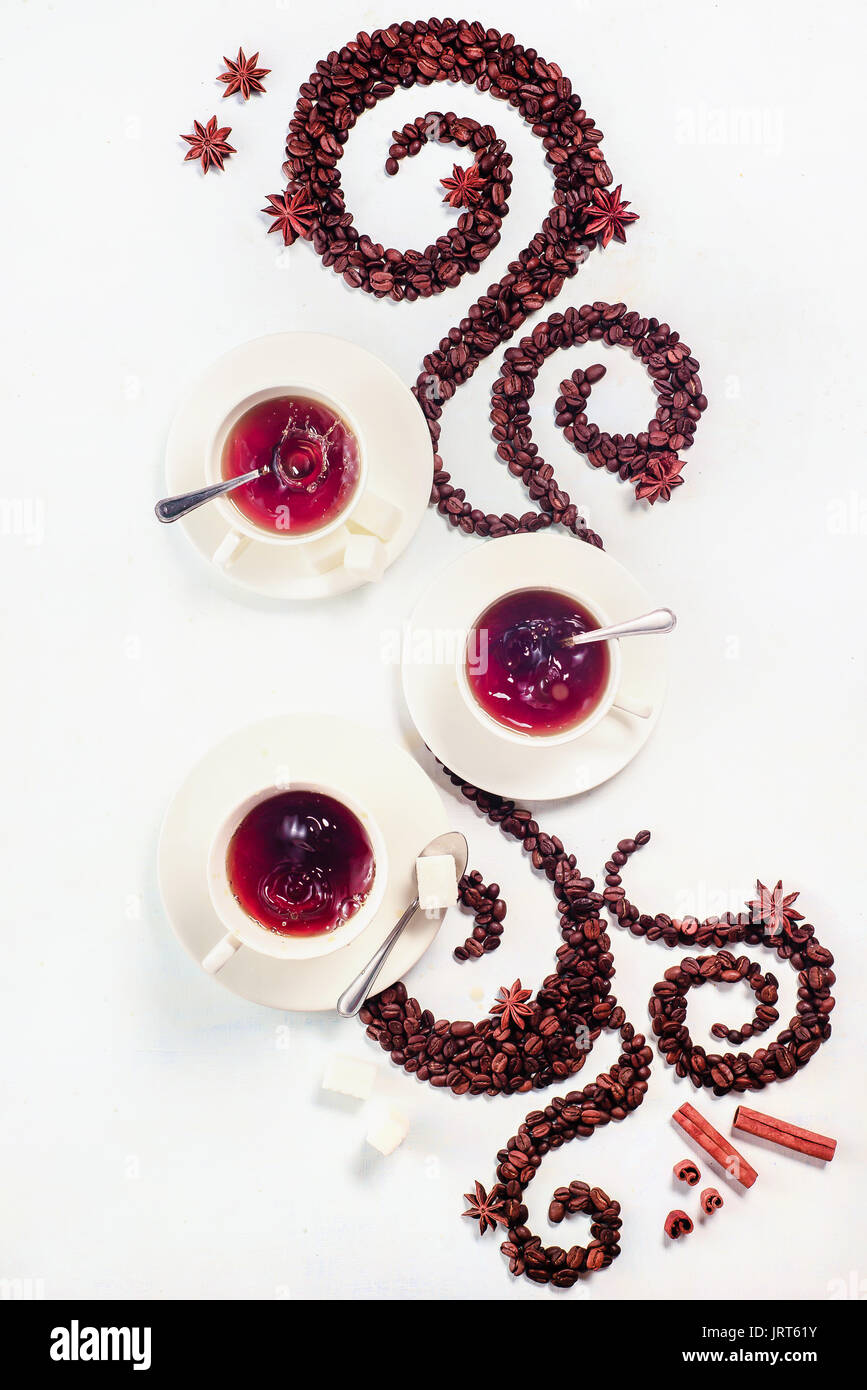 Les grains de café allongé en forme d'un tourbillon avec la coupe, la cannelle, l'anis étoile et les beignes sur un fond blanc Banque D'Images