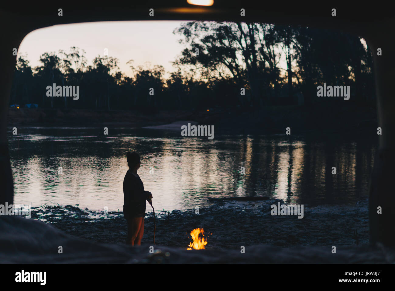 Camp de l'après-midi par le fleuve Murray dans la lumière dorée avec une femme ayant tendance à l'incendie à la recherche de la voiture familiale. Banque D'Images