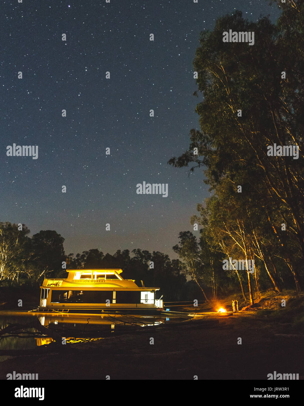 Péniche stationnée sur la Murray River dans la nuit sous les étoiles avec un feu de camp sur les rives près de Echuca. Banque D'Images