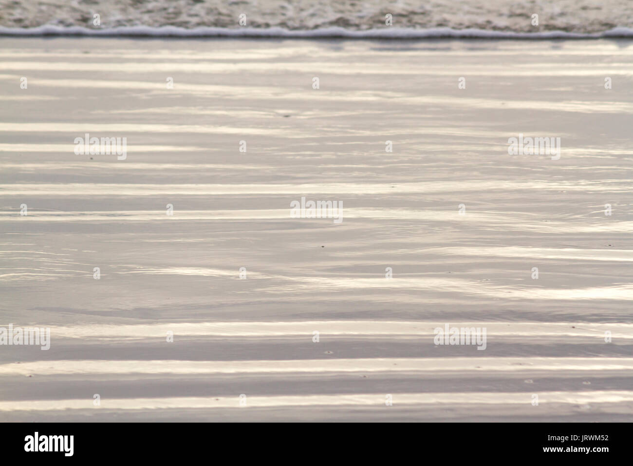 Fermer à la photographie des motifs abstraits sur la plage créé par le sable humide et petites vagues en fin d'après-midi soleil Banque D'Images Fermer à la photographie des motifs abstraits sur la plage créé par le sable humide et petites vagues en fin d'après-midi soleil Banque D'Images
