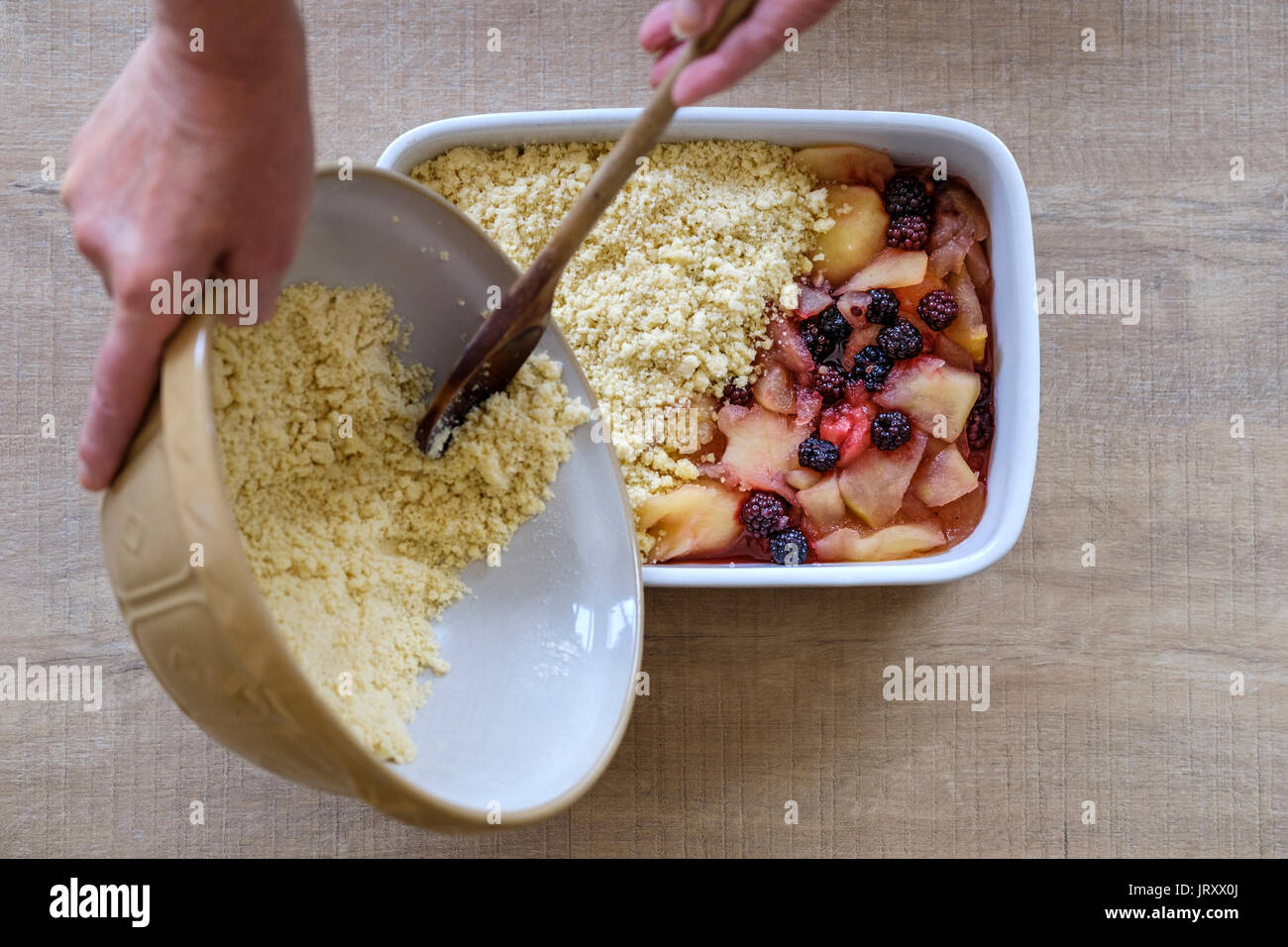 Un cuisinier prépare et ajoute le crumble mélanger à un traditionnel français apple et blackberry pudding Banque D'Images