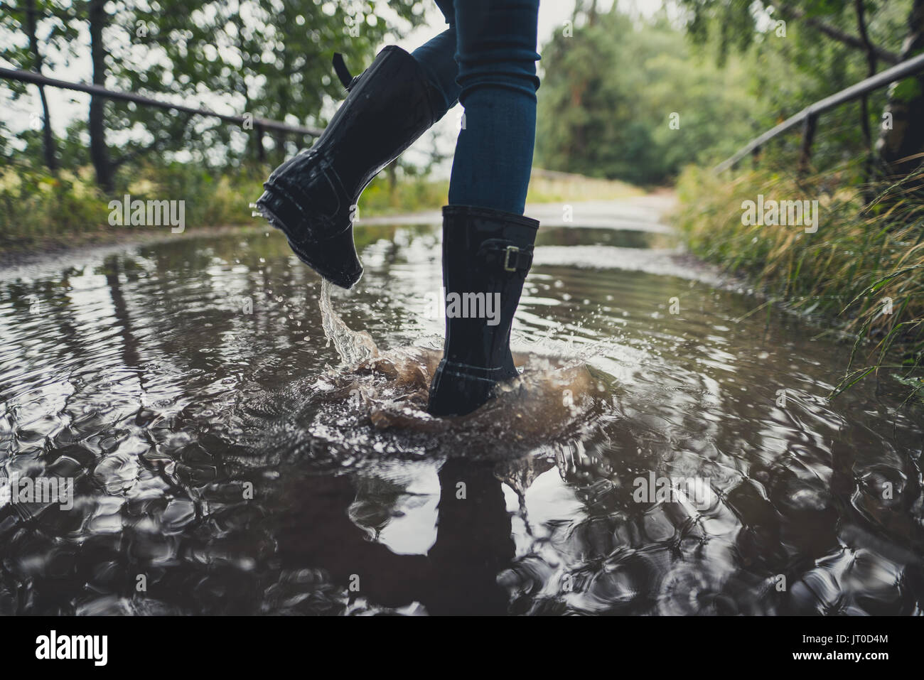 Close-up of young woman's legs avec des bottes en caoutchouc de saut et de danser dans une flaque Banque D'Images