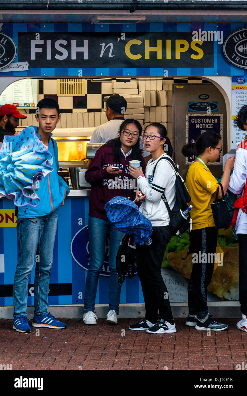 Les jeunes touristes à l'abri de la pluie à l'extérieur d'un poisson et Chip Shop sur le front de mer de Brighton, Brighton, Sussex, UK Banque D'Images