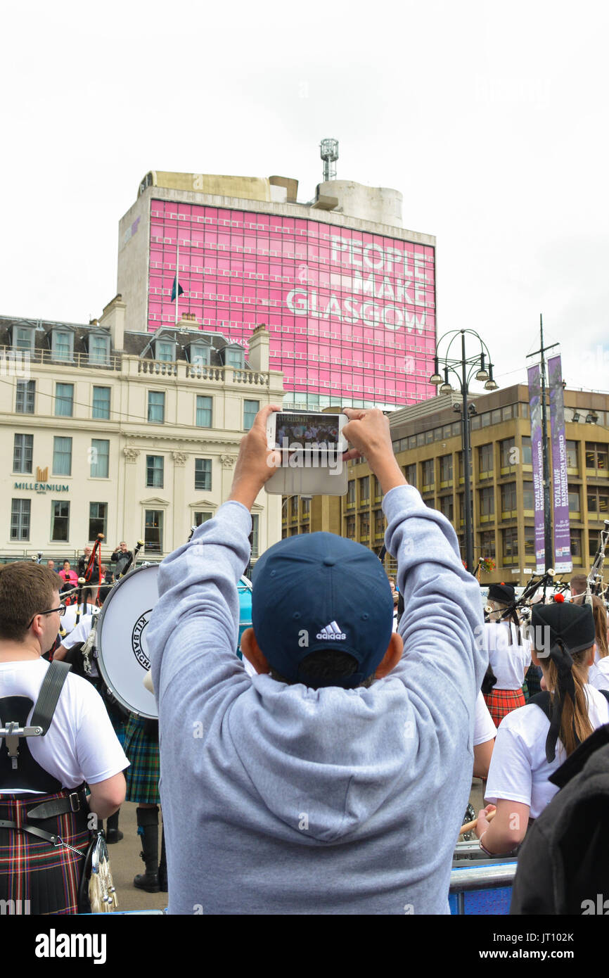 L'homme d'atteindre jusqu'à un film de pipe band à Glasgow Banque D'Images