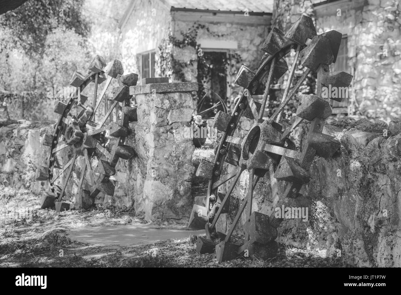 Une paire de roues en acier antique d'un vieux tracteur, décorant la porte grâce à une vieille clôture en pierre à un rock house. Banque D'Images