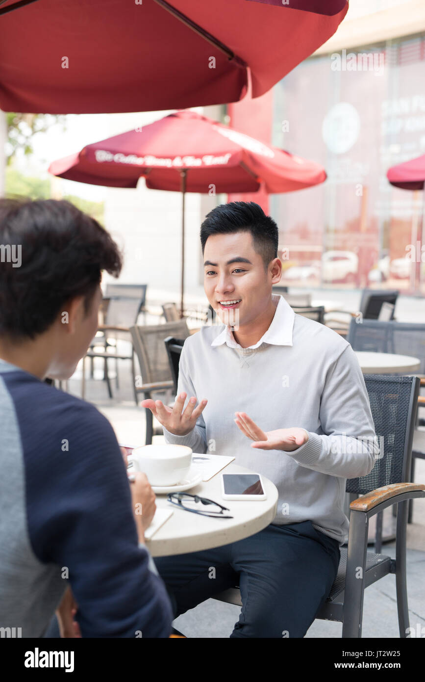 Deux jeunes hommes d'affaires dans les tenues de beau sourire, parler, boire du café pendant que working in office Banque D'Images
