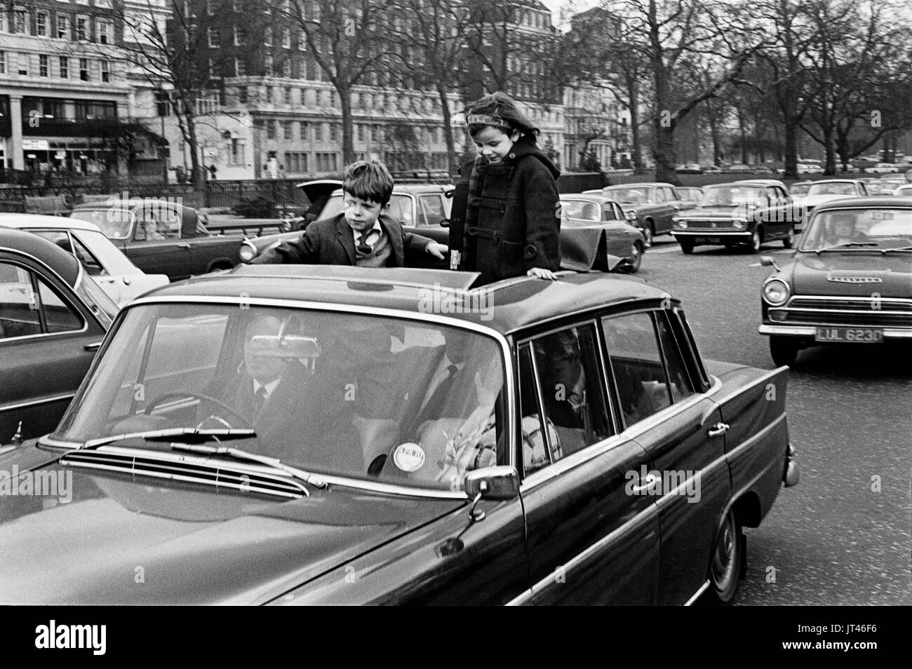 Les enfants britanniques des années 1970 debout sur des sièges d'auto, se tiennent à travers le toit ouvrant tandis que la voiture est conduite dans la circulation londonienne. Park Lane, Londres Angleterre 1970 HOMER SYKES Banque D'Images