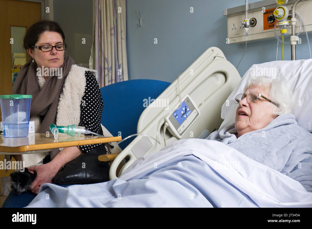 Une vieille dame dans un lit d'hôpital en attente d'un paquet de soins pour permettre sa libération la visite d'un membre de la famille.. Banque D'Images