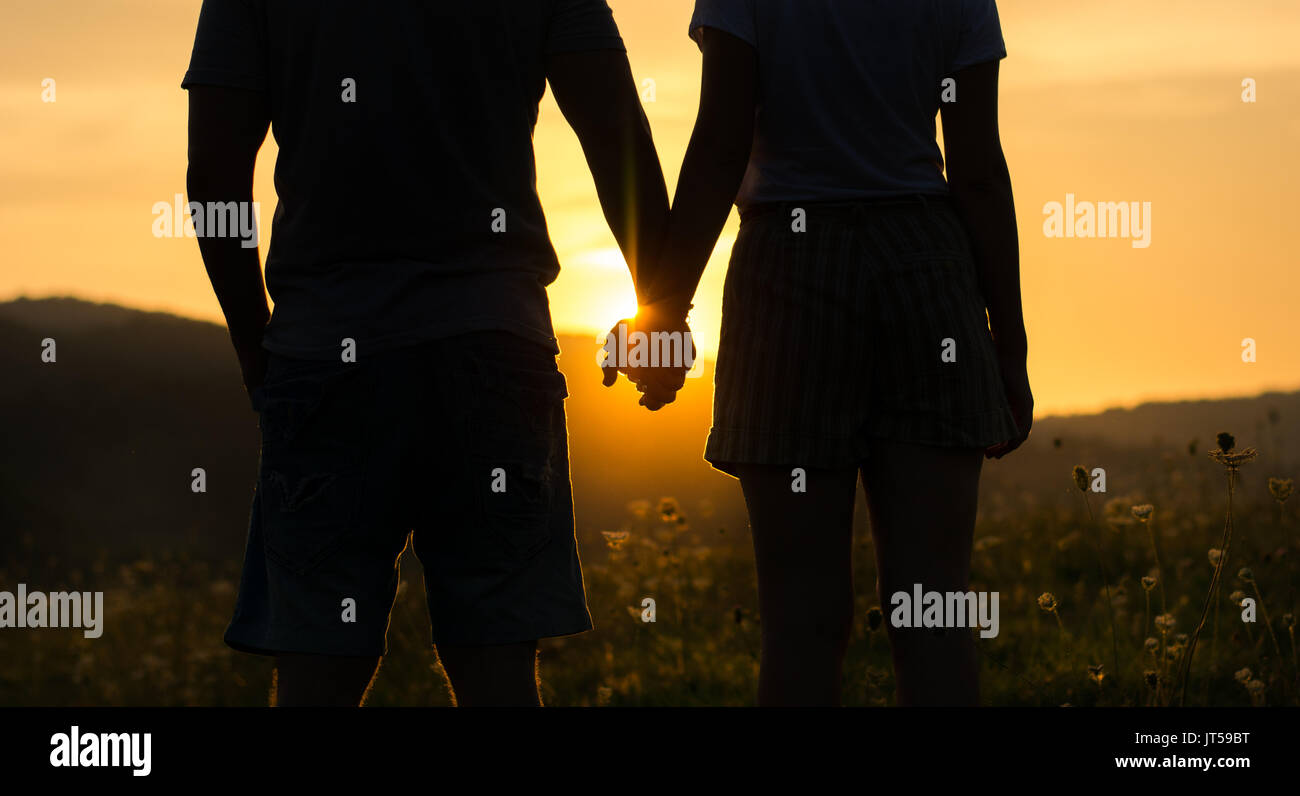 Couple holding hands et regarder le coucher du soleil, la silhouette romantique Banque D'Images
