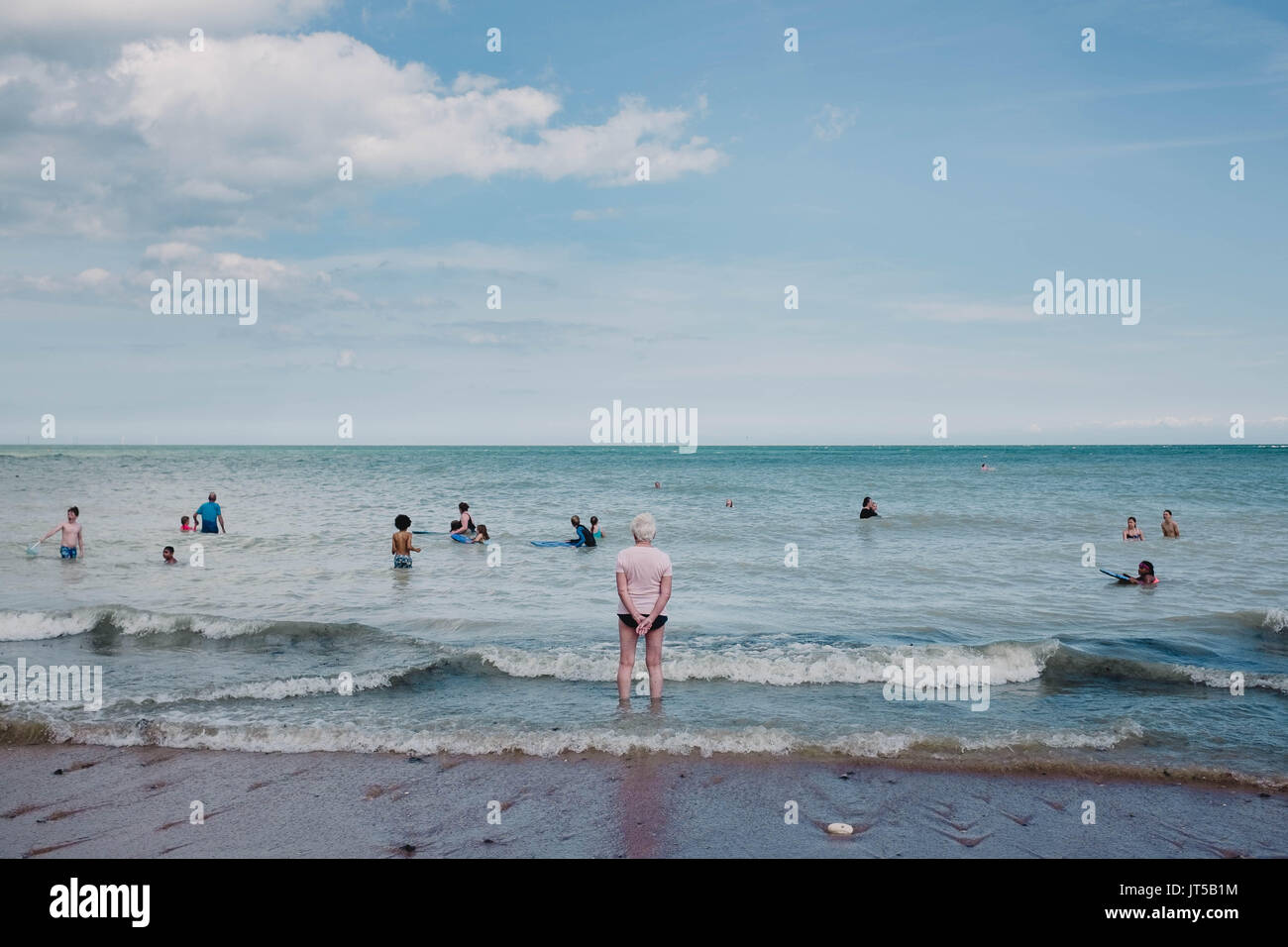 Une dame âgée palettes dans la mer à l'extérieur au-delà les jeunes nageurs sur un jour d'été. Banque D'Images