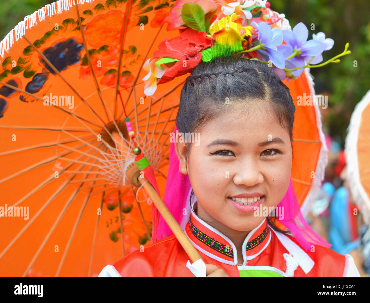 Jolie fille chinoise thaïlandaise dans une robe traditionnelle avec des sourires de parasol orange pour l'appareil photo. Banque D'Images