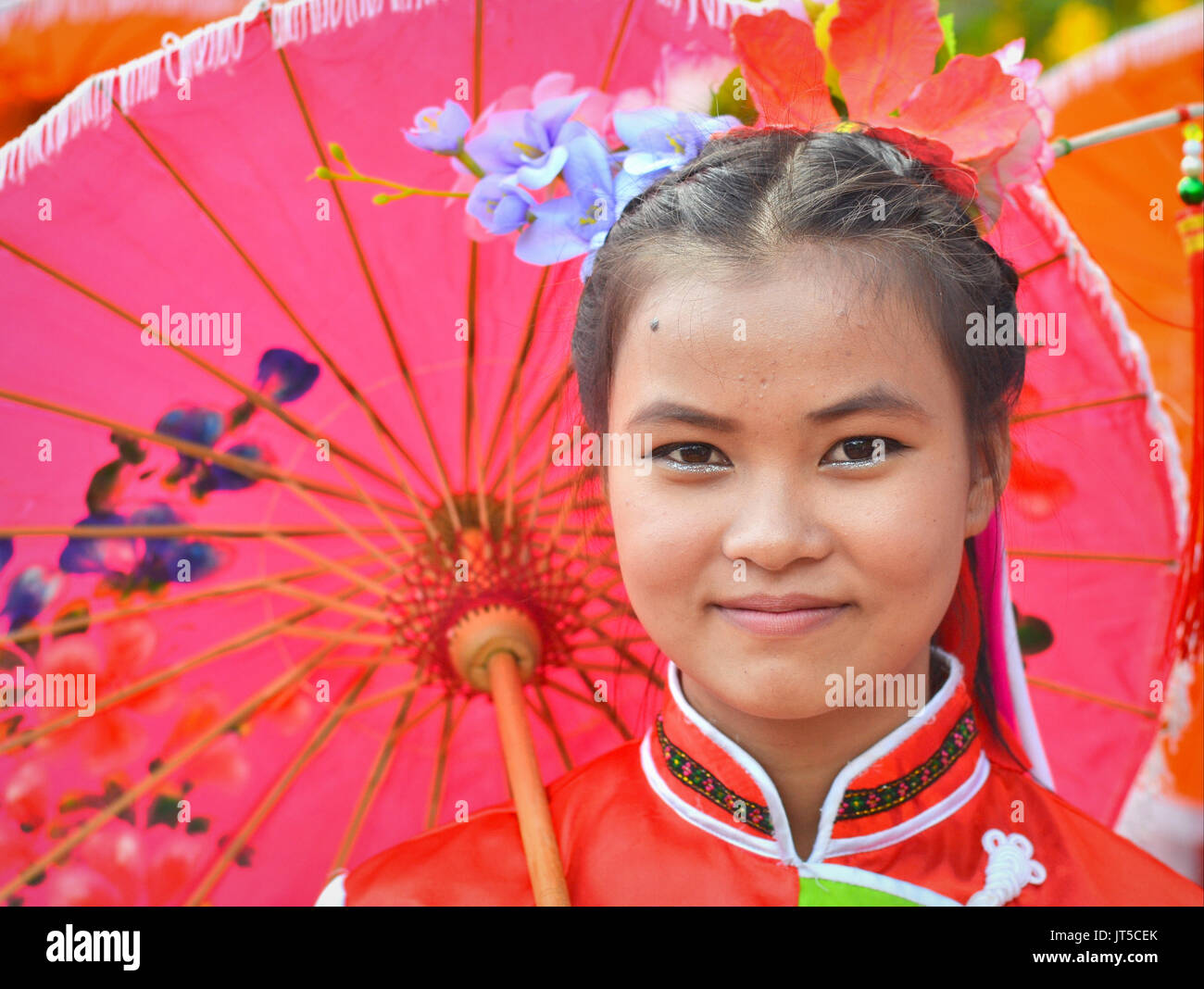 Jolie fille chinoise thaïlandaise dans une robe traditionnelle avec des poses de parasol rouges pour l'appareil photo. Banque D'Images