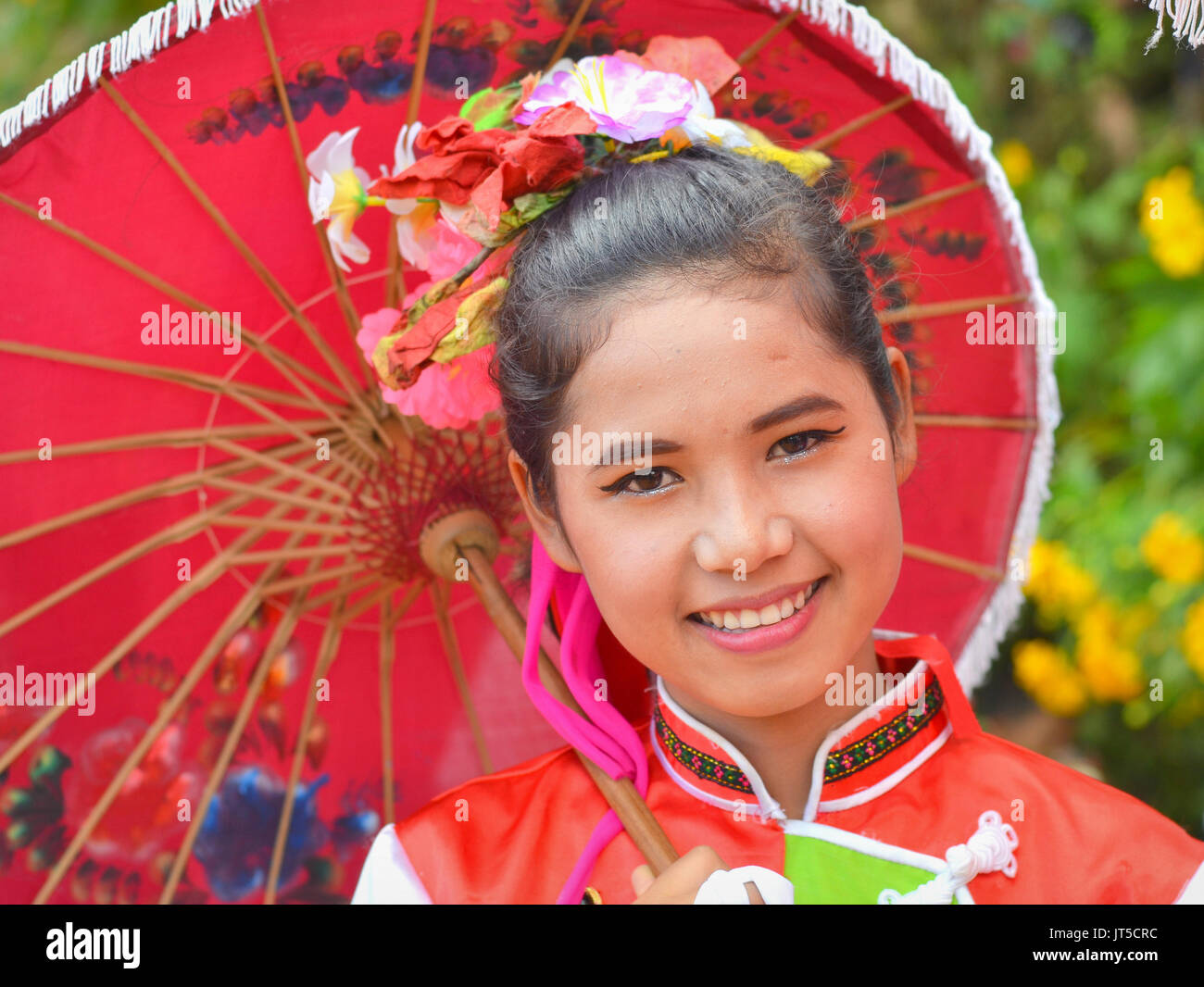 Jolie fille chinoise thaïlandaise dans une robe traditionnelle avec des sourires de parasol rouge pour l'appareil photo. Banque D'Images