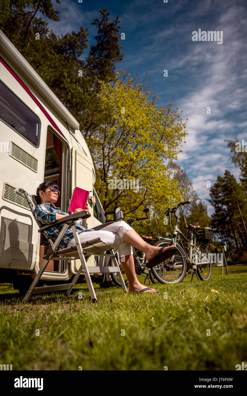 Femme se détend et lit un livre à côté du camping . Location caravane Vacances. Vacances famille vacances, voyages voyage en camping-car. Banque D'Images