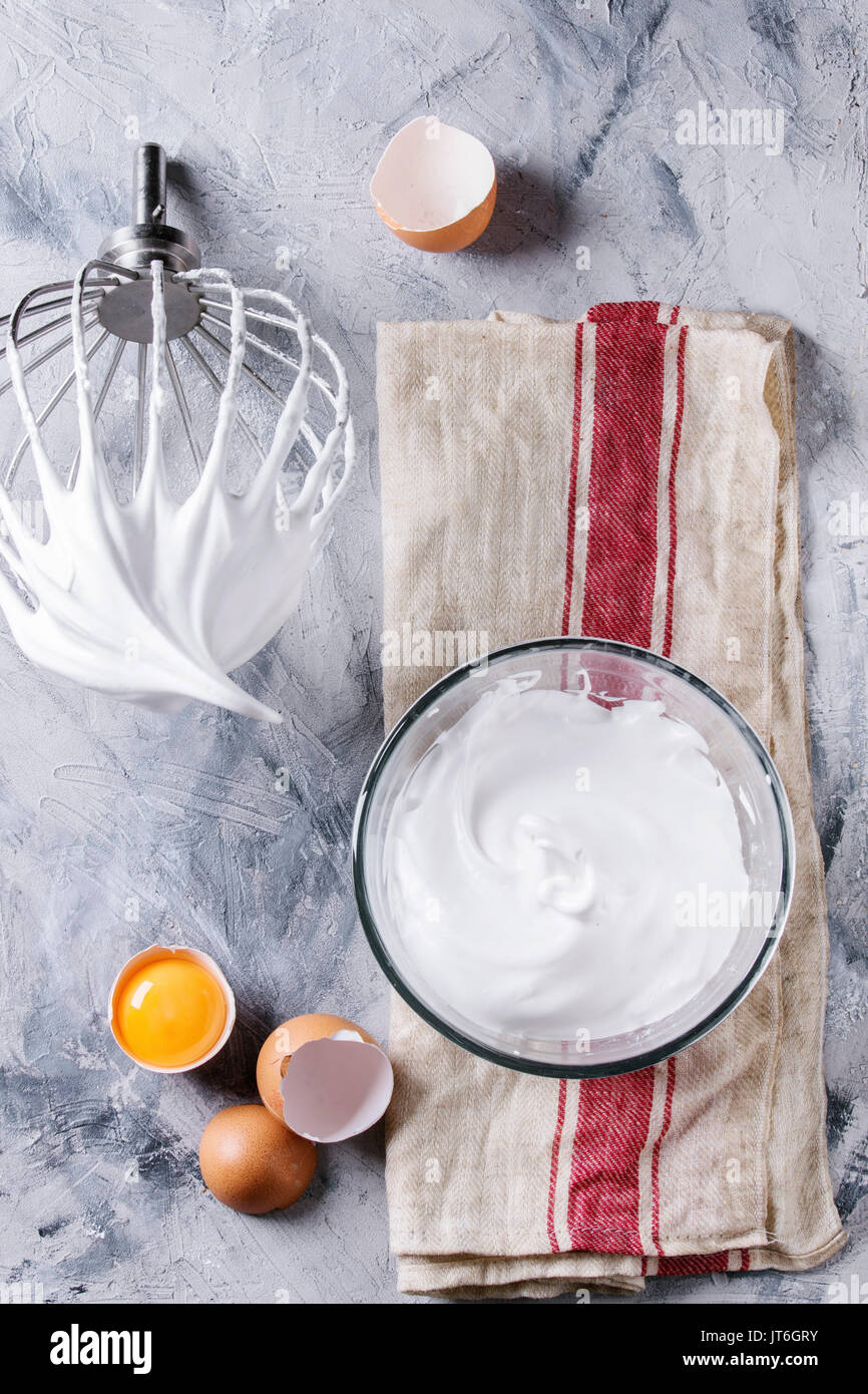 Processus de la cuisson de la meringue. Les blancs d'œufs fouettés avec fouet mélangeur sur oeufs cassés sur lin gris serviette sur fond de texture. Vue d'en haut. Pâtisseries Dessert Banque D'Images