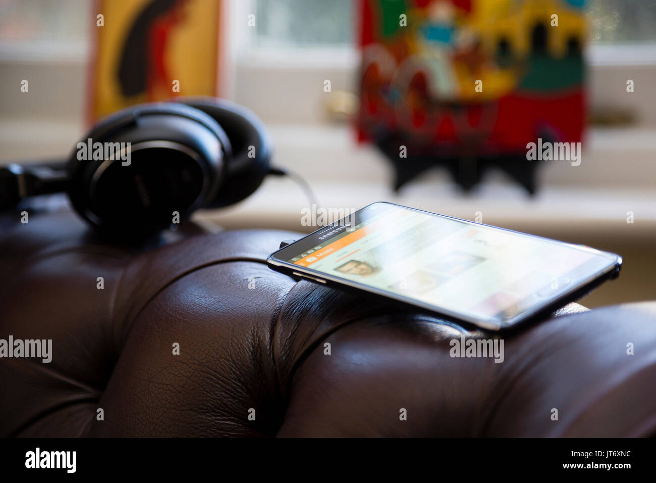 Londres, Royaume-Uni. Samsung smartphone avec paire d'écouteurs de bras assis sur un fauteuil en cuir luxueux. Banque D'Images