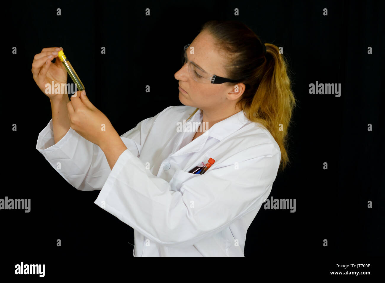 Une jeune femme examine des tubes à essai remplis de liquides colorés sur fond noir. Banque D'Images
