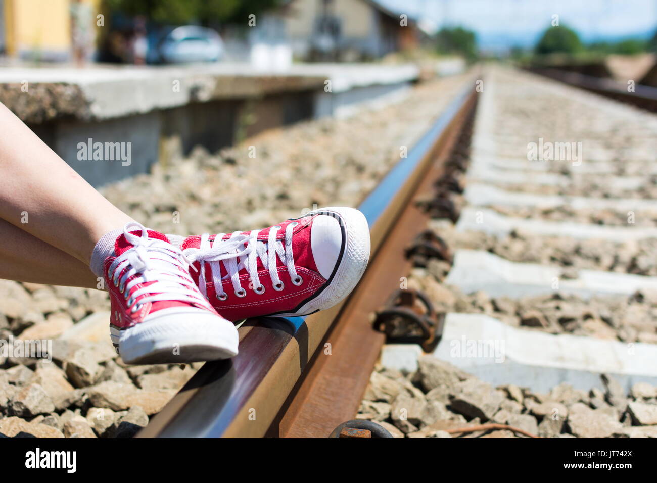 Pieds de fille en rouge sneakers assis par le chemin de fer Banque D'Images