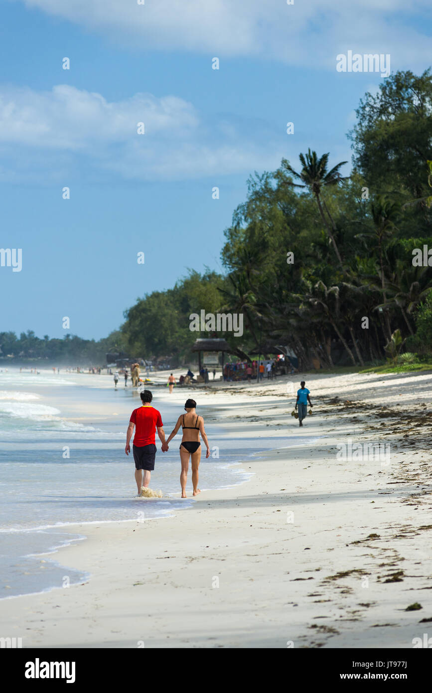 Un couple marche le long de la plage de sable blanc tropicales sur la rive d'une journée ensoleillée, Diani, Kenya Banque D'Images
