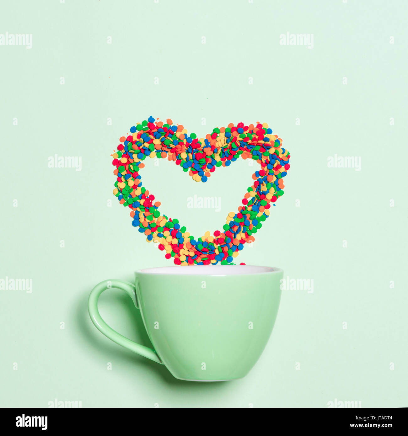 Tasse de Cappuccino avec le symbole en forme de coeur et des bonbons sur fond vert pastel Banque D'Images