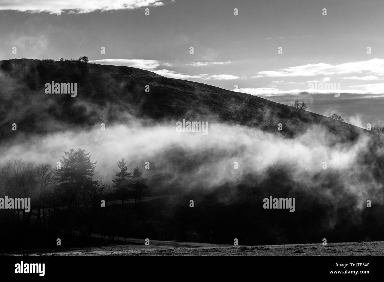 Montagne avec un nuage très bas cachent partiellement quelques arbres et une route Banque D'Images